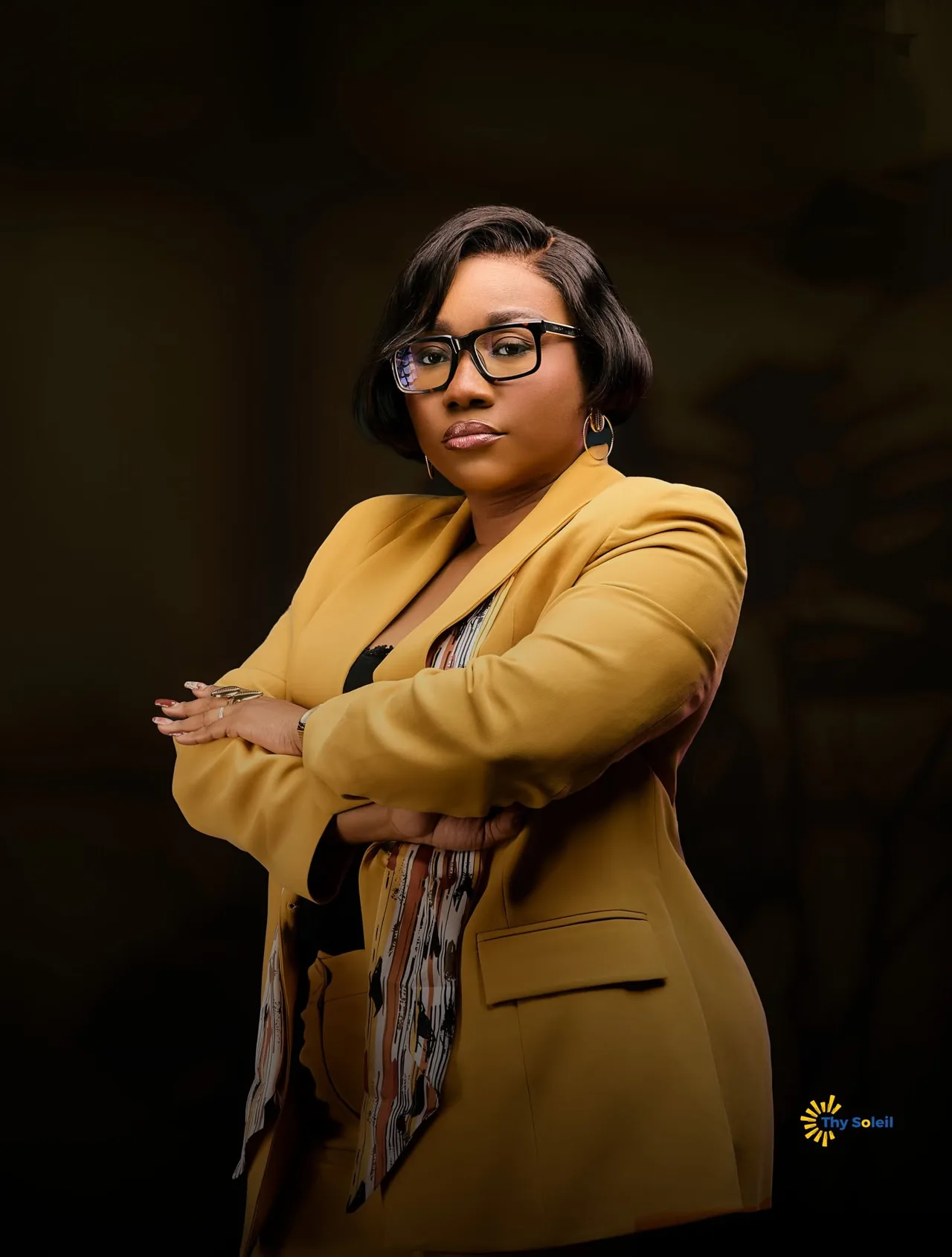 Portrait en studio d’une femme portant une veste ocre et des lunettes.