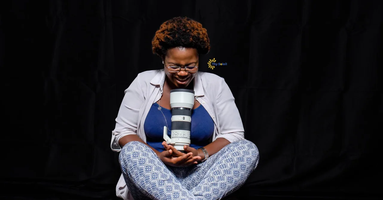 Une photographe assise tient un grand téléobjectif devant un fond noir.